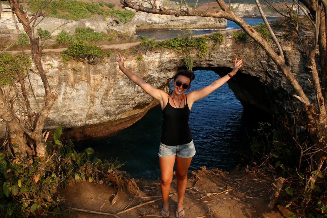 ruta por indonesia chica posando en un acantilado con los brazos abierto sonriendo a la cámara